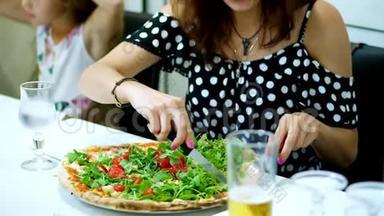 在披萨里，一个女人切了一个大的，多汁的，热的披萨，里面有绿色的，和樱桃番茄。 一块一块的披萨